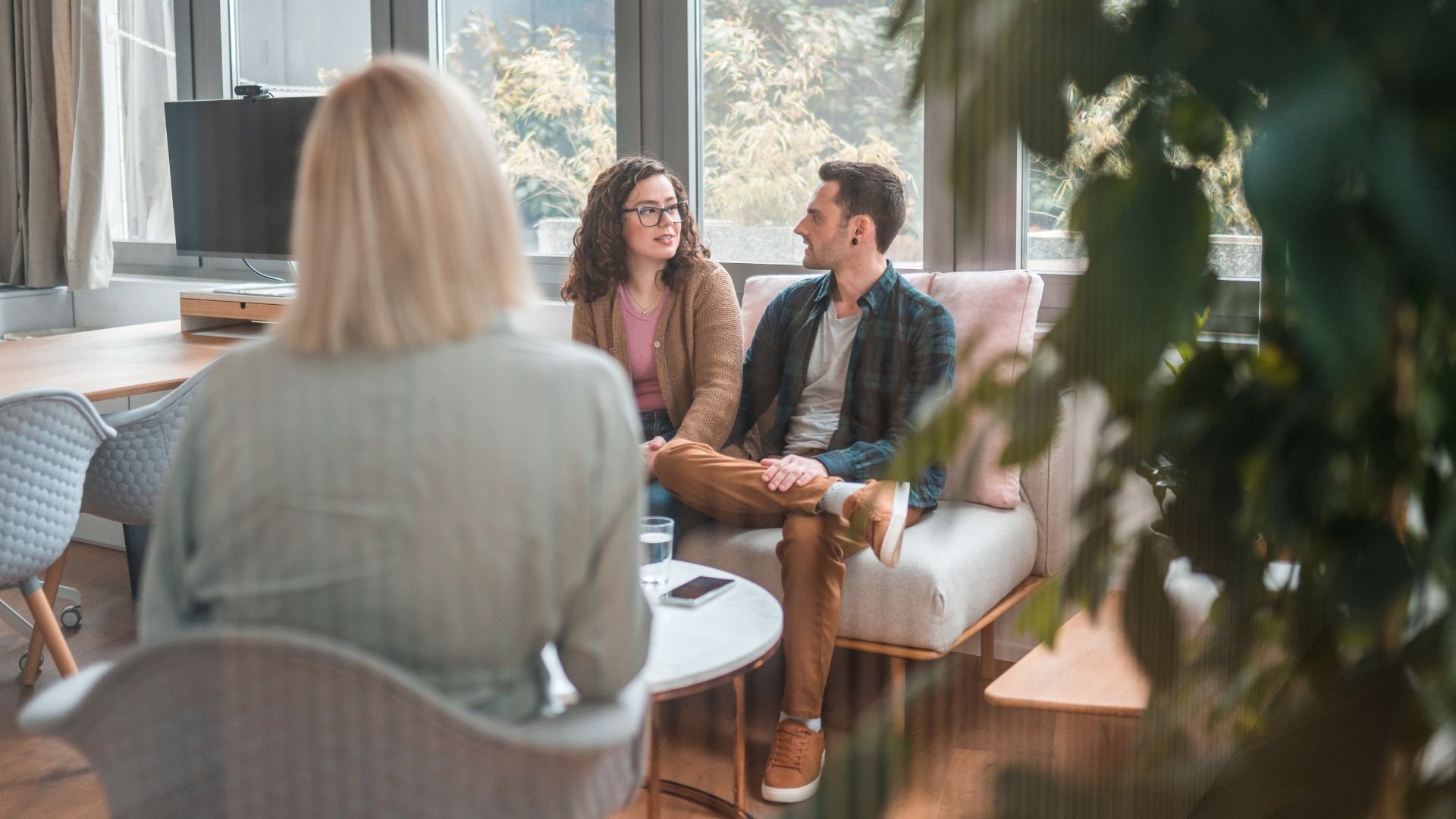 Counseling session with couple holding hands in bright, plant-filled room