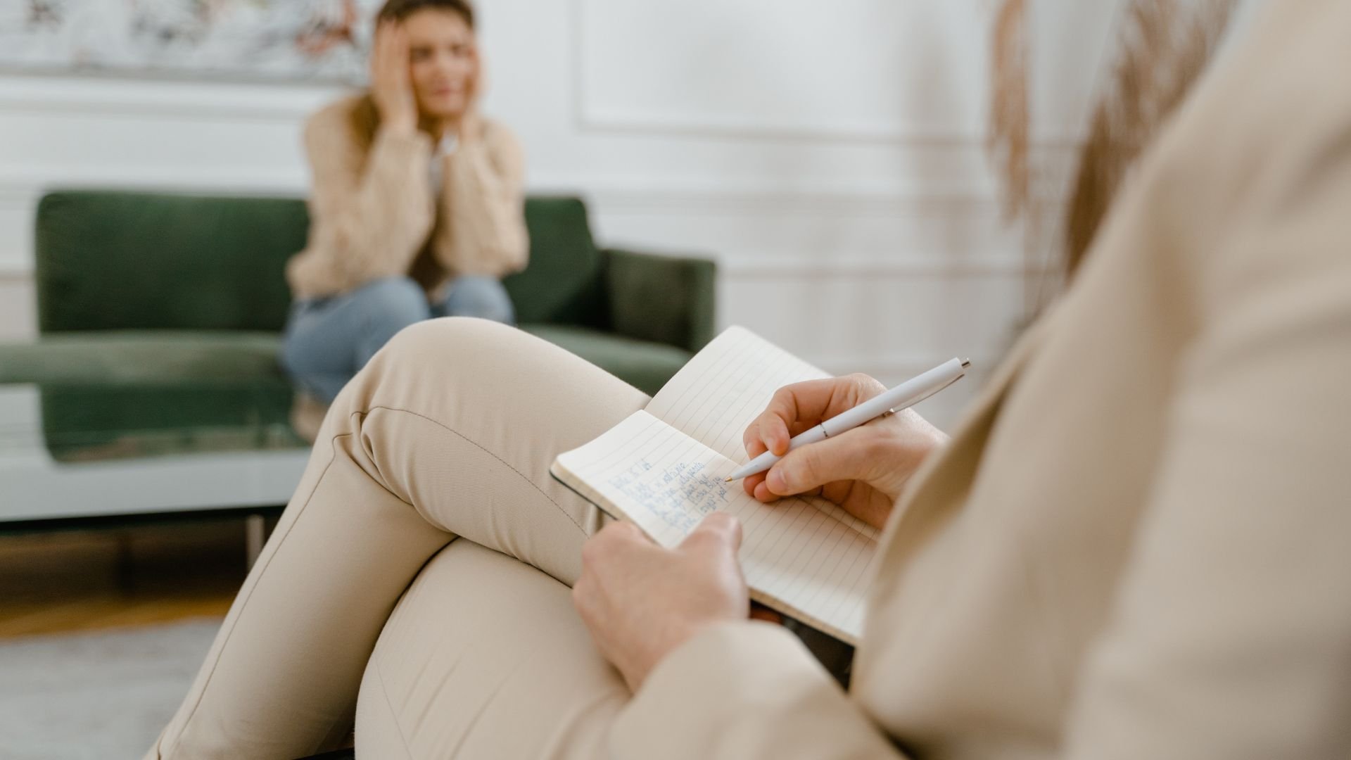 Therapist taking notes while person sits distressed on green couch