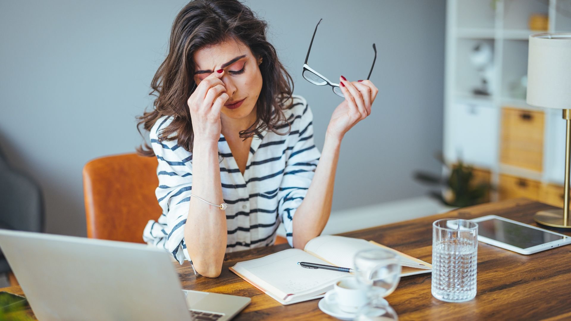 Stressed woman rubbing eyes while working at desk with laptop